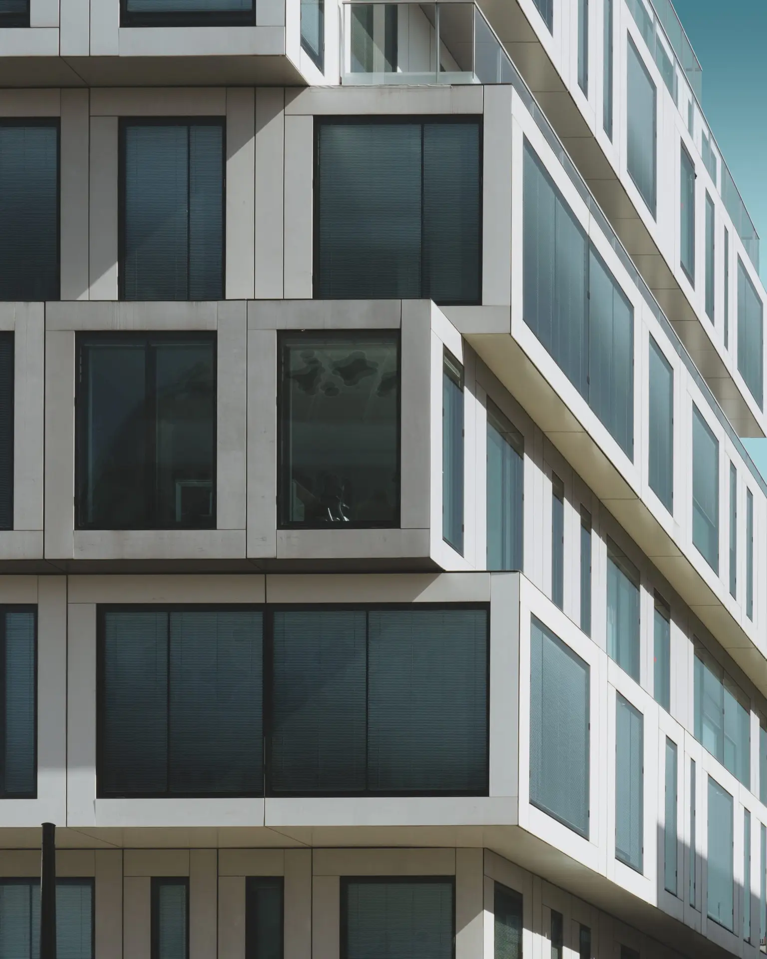 A vertical shot of a grey concrete building with big windows under the blue sky